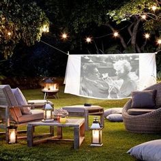 an outdoor movie is set up in the grass with lights strung over it and furniture