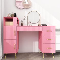 a pink desk with gold handles and drawers in front of a wall mounted vanity mirror