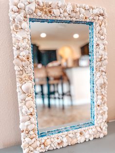 there is a mirror made out of shells on the table and chairs in the background