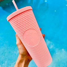 a hand holding a pink starbucks cup next to a pool