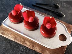 three red desserts with raspberries are on a tray