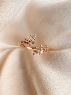 a gold ring with two leaves on it sitting on top of a white satin fabric