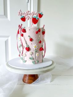 a pink cake decorated with strawberries and daisies on a white plate next to a door