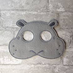 a gray mask with two holes in the middle on a brick wall behind it is a grey hippo face