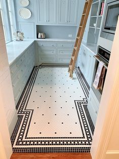 a kitchen with white cabinets and black and white floor tiles on the floor is a ladder in the middle of the room