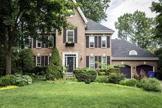 a large brick house with black shutters on the front and side windows, surrounded by lush green grass