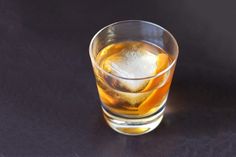 a glass filled with ice and an orange slice on top of a black tablecloth