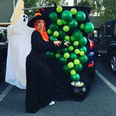 a woman dressed as a witch with green balloons