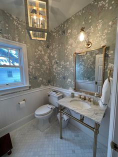 a bathroom with a toilet, sink and mirror next to a window on the wall