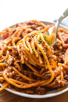 a plate full of spaghetti with meat and cheese on it, being held by a fork