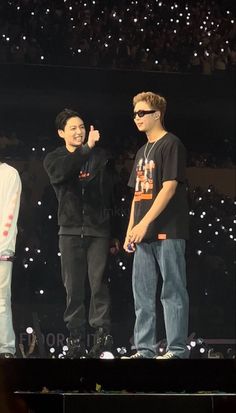 two young men standing on top of a stage with one giving the thumbs up sign