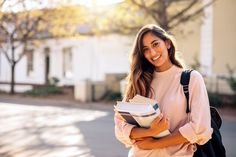 a beautiful young woman holding a book and smiling at the camera while standing in front of a