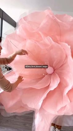 a woman is standing in front of a giant pink flower with her hands on the petals