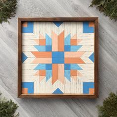 a wooden frame with an orange, blue and white star design on the inside is surrounded by pine branches