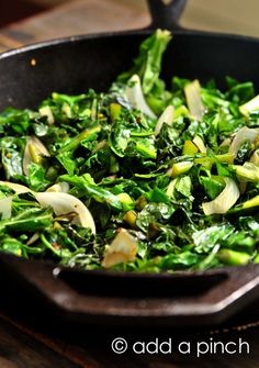 a pan filled with greens and onions on top of a table