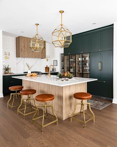 a kitchen island with four stools in front of it and two hanging lights above the island