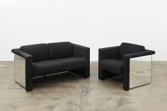 two black couches sitting next to each other on a cement floor in front of a white wall