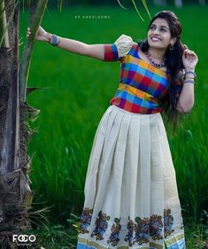 a woman standing next to a palm tree wearing a colorful shirt and skirt with her hands on her hips