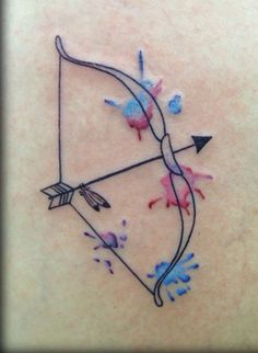 an arrow tattoo on the back of a woman's left shoulder, with paint splatters all over it