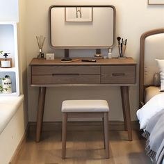 a desk with a mirror and stool in a small room next to a bed that has white sheets on it