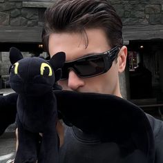 a man in sunglasses holding a black cat stuffed animal