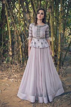 a woman standing in front of bamboo trees wearing a long dress with an embellishment on the waist