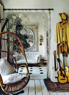 a room with white walls and wooden flooring has guitars on the wall next to a wicker swing chair