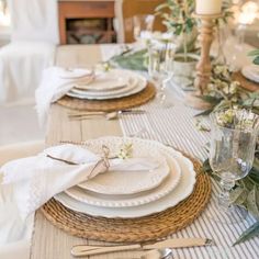 the table is set with white plates and silverware, napkins and greenery