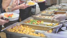 many people are serving themselves food at a buffet