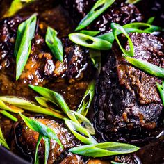 some meat and green onions are cooking in a skillet with sauce on the side