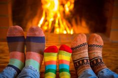 three pairs of colorful socks sitting in front of a fire place with their feet up