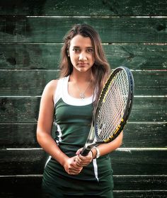 a woman holding a tennis racket in front of a wooden wall with planks