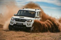 a white four - door suv driving through the desert with dust coming off it's tires