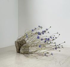 a sculpture made out of twigs and flowers on the floor in front of a white wall