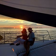 a man and woman sitting on the back of a boat in the ocean at sunset