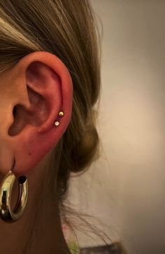 a close up of a woman's ear with two small gold hoops on it