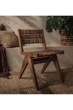 a wooden chair sitting in front of a wall next to a potted plant and pillows