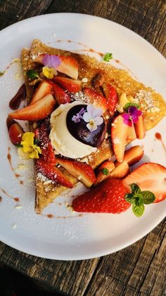 a white plate topped with crepes covered in strawberries and other toppings