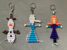 three key chains made to look like legos are sitting on the floor, one has an orange and white beaded figure