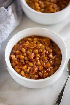 two white bowls filled with baked beans on top of a table