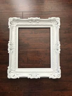 an empty white frame sitting on top of a wooden floor