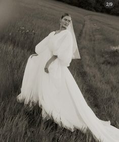 a black and white photo of a woman in a wedding dress standing in tall grass