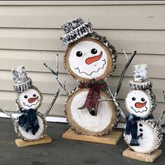 three snowmen with hats and scarfs made out of wood logs sitting in front of a house