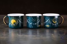 three coffee mugs with mountains and stars painted on them, sitting next to each other