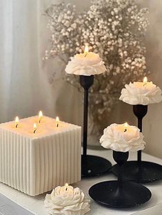 three candles are sitting on a table with flowers in front of them and one candle is lit