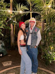 a man and woman standing next to each other in front of palm trees at night