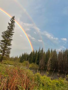 two rainbows in the sky over a river and forest with tall trees on both sides