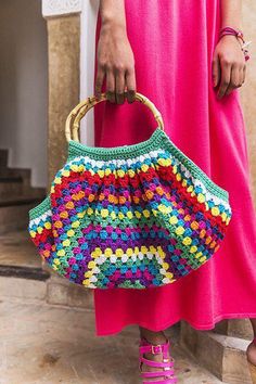 a woman in pink dress holding a multicolored crocheted purse with gold handles