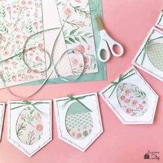 some cards and scissors on a pink surface with flowers, leaves and hearts hanging from them