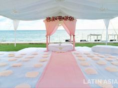 an outdoor wedding setup with white linens and pink flowers on the aisle, overlooking the ocean